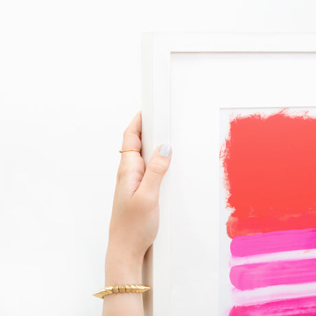 Hand holding red and pink abstract art in white frame at angle