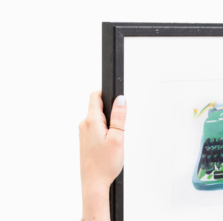 Hand holding green typewriter art in riveted black frame at angle
