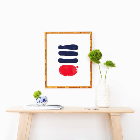 Navy and red abstract art in gold bamboo frame above table with plants and vases